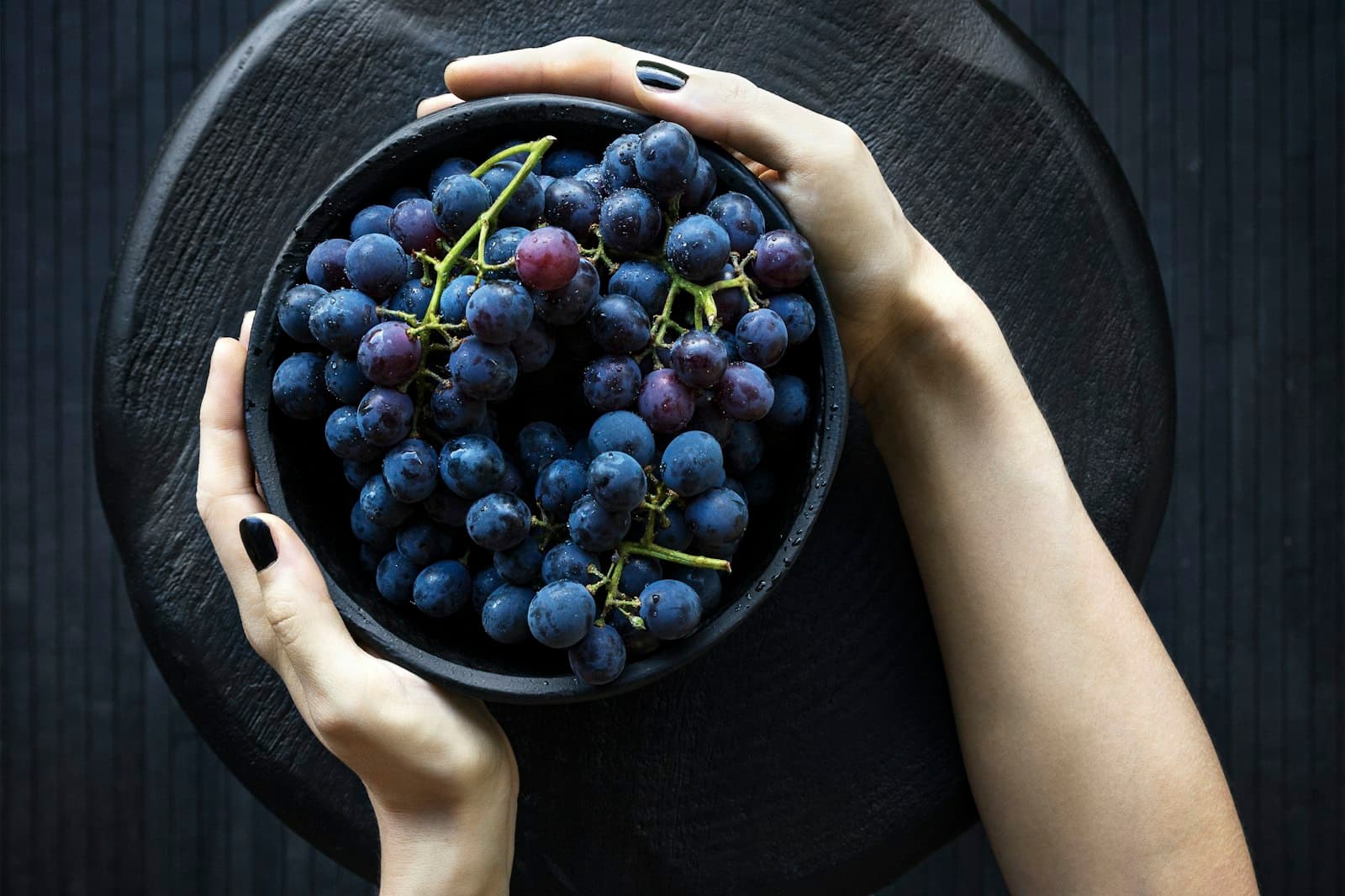 Manos sosteniendo un tazón de frutas frescas y vibrantes bajo una luz cálida.