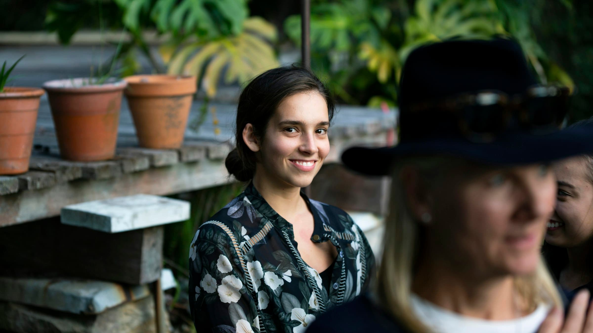 Grupo de personas sonriendo y conversando en un jardín exuberante, bajo una luz cálida al atardecer.