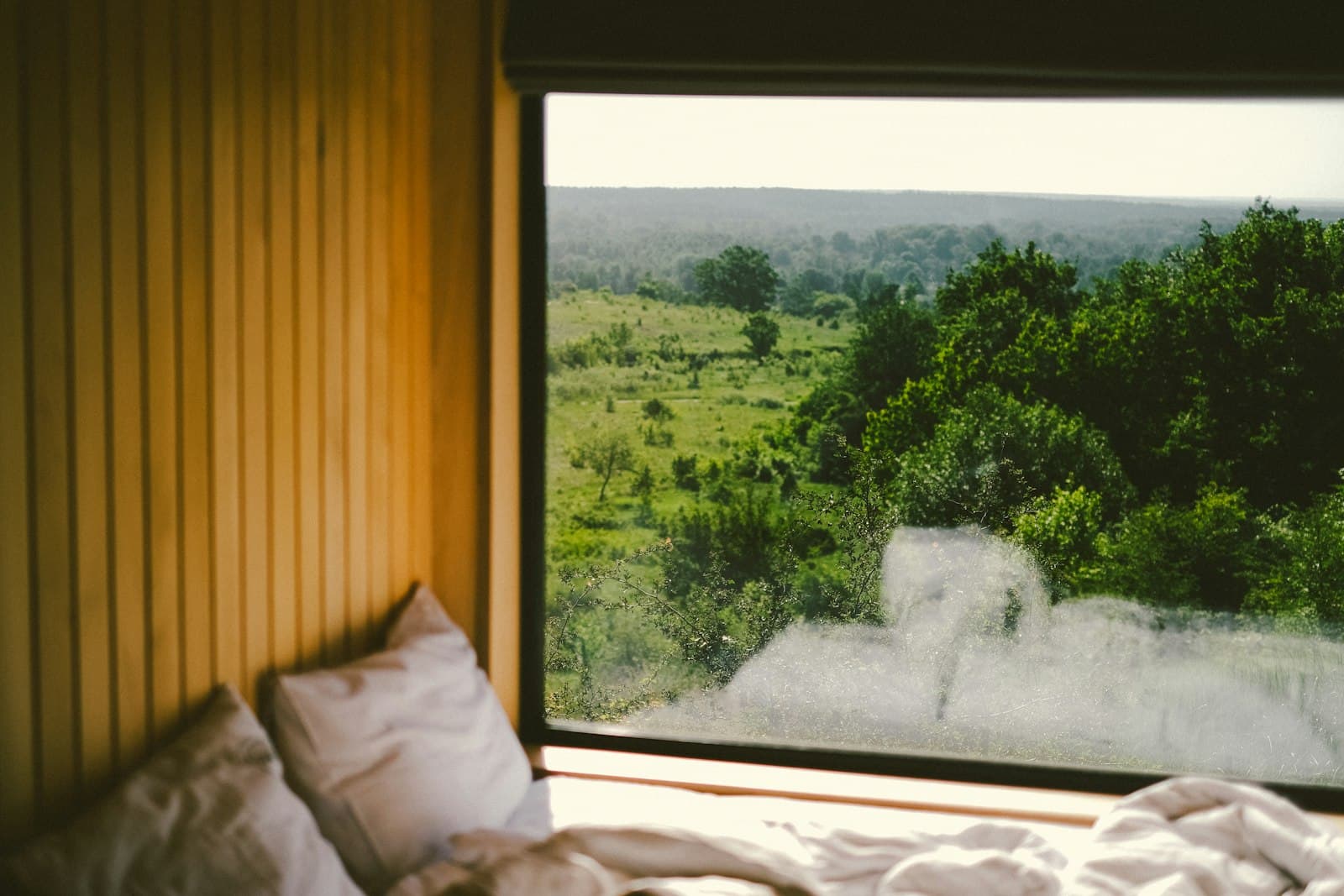 Dormitorio con una gran ventana que da a un paisaje natural, decorado en tonos neutros para fomentar la relajación.