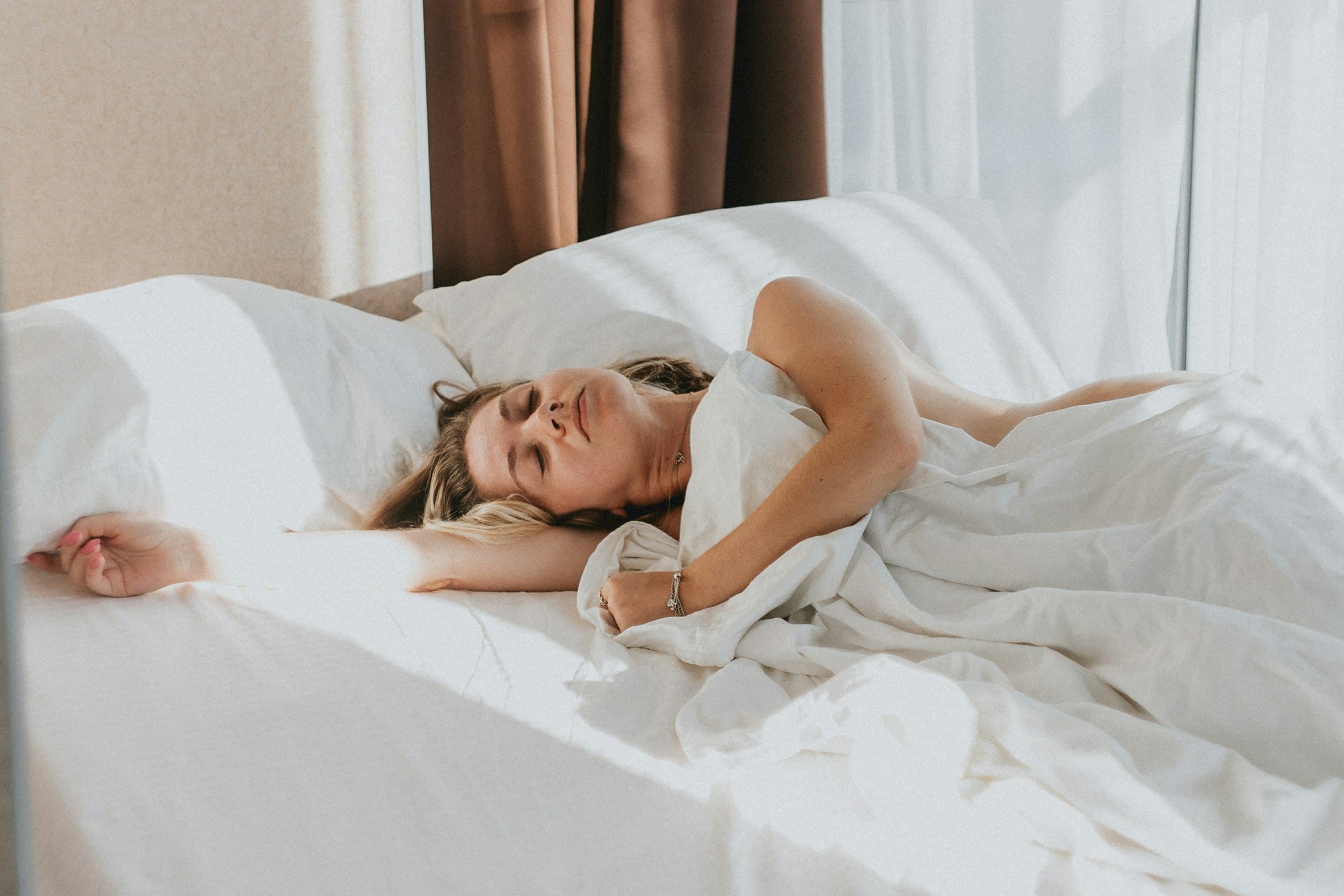 Una mujer serena durmiendo tranquilamente en una cama con luz suave de la mañana