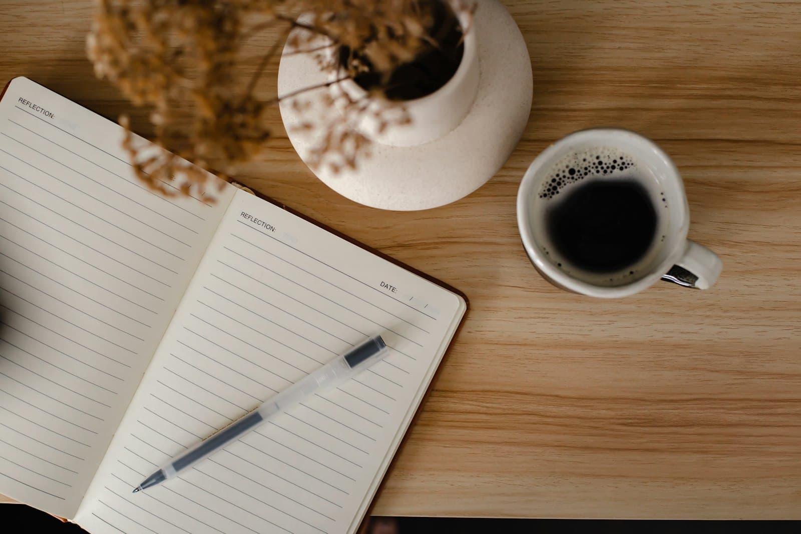 Un diario abierto con una pluma al lado y una taza de café humeante en una mesa de madera.