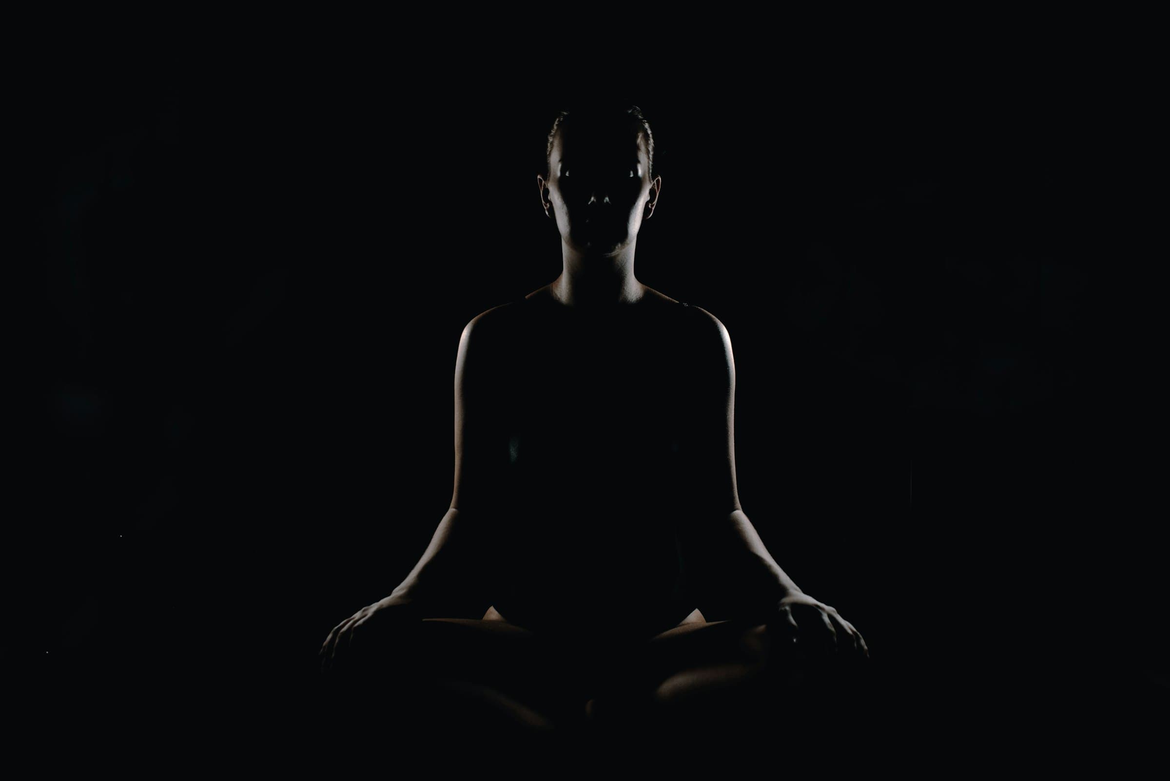Una persona sentada en posición de meditación en un espacio tranquilo y luminoso, con las manos apoyadas en las rodillas.