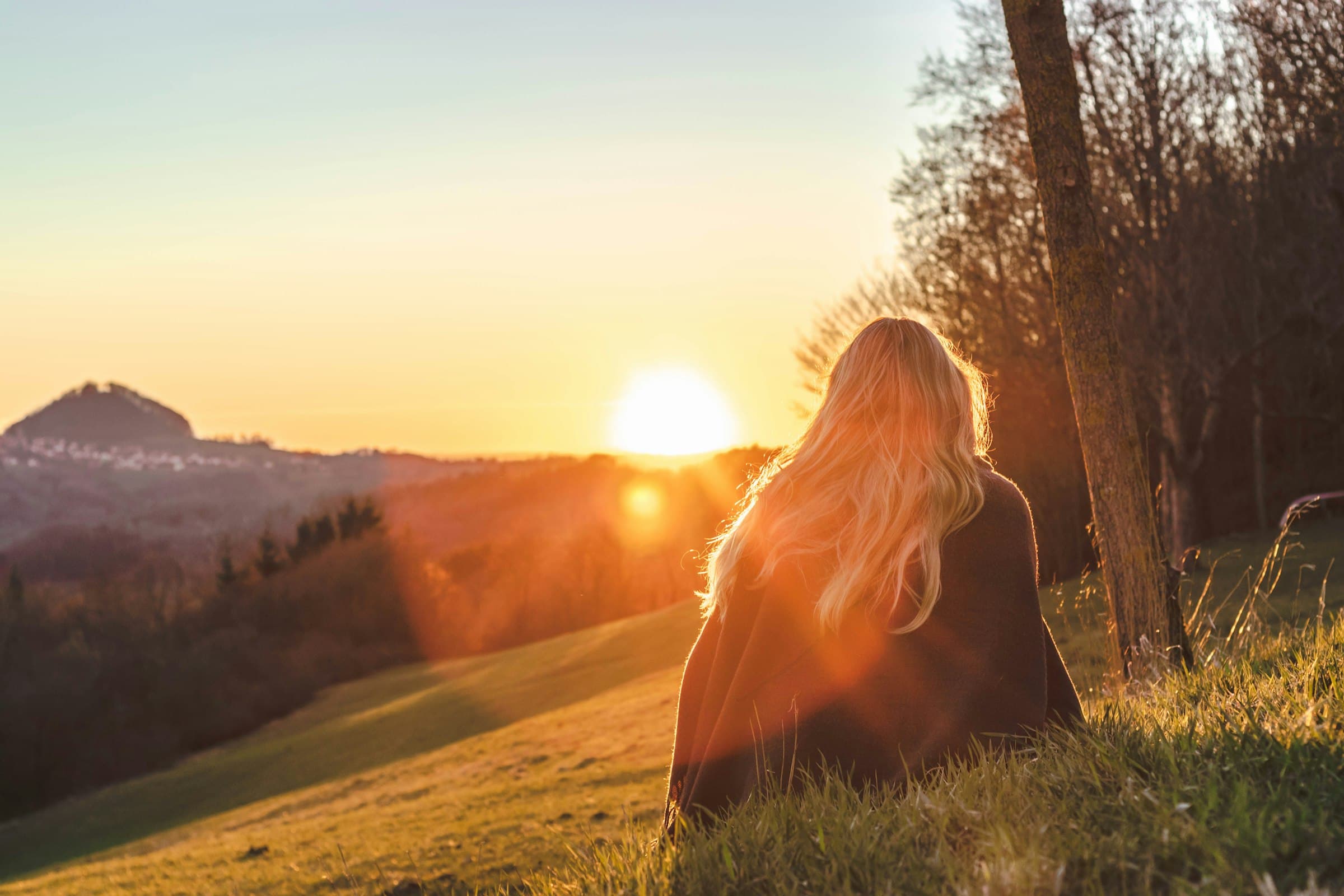 Una mujer serena meditando al amanecer en un entorno natural exuberante, con luz dorada.