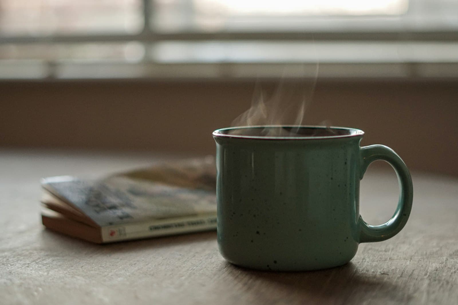 Una taza de té humeante colocada sobre una superficie de madera, con la luz cálida de la mañana entrando por una ventana.