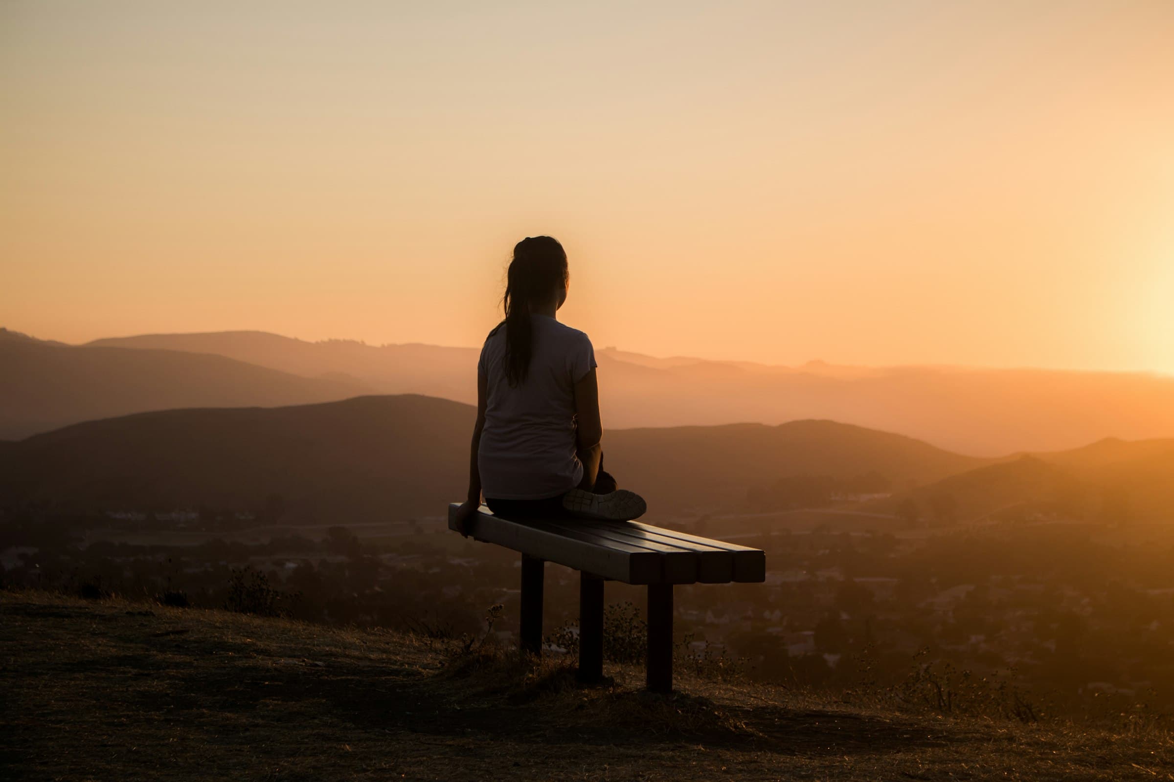 Una mujer serena meditando al amanecer con una taza de té, rodeada de luz suave.