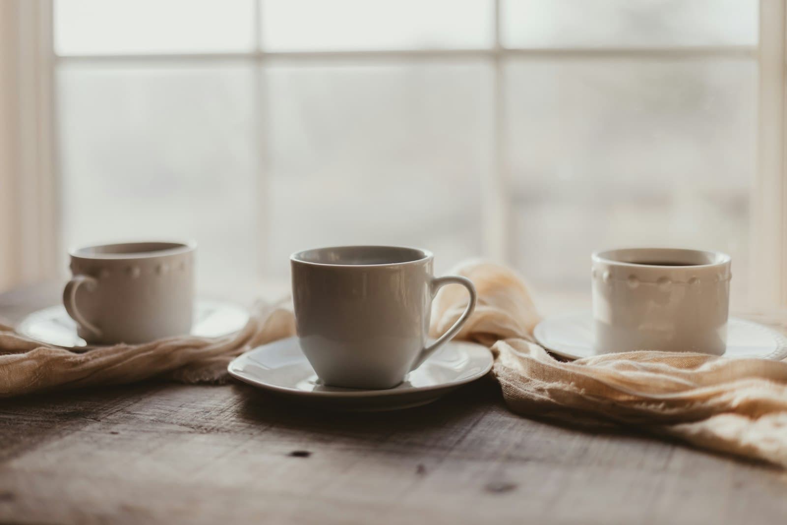 Una taza de té humeante junto a una ventana con vistas a un paisaje otoñal.