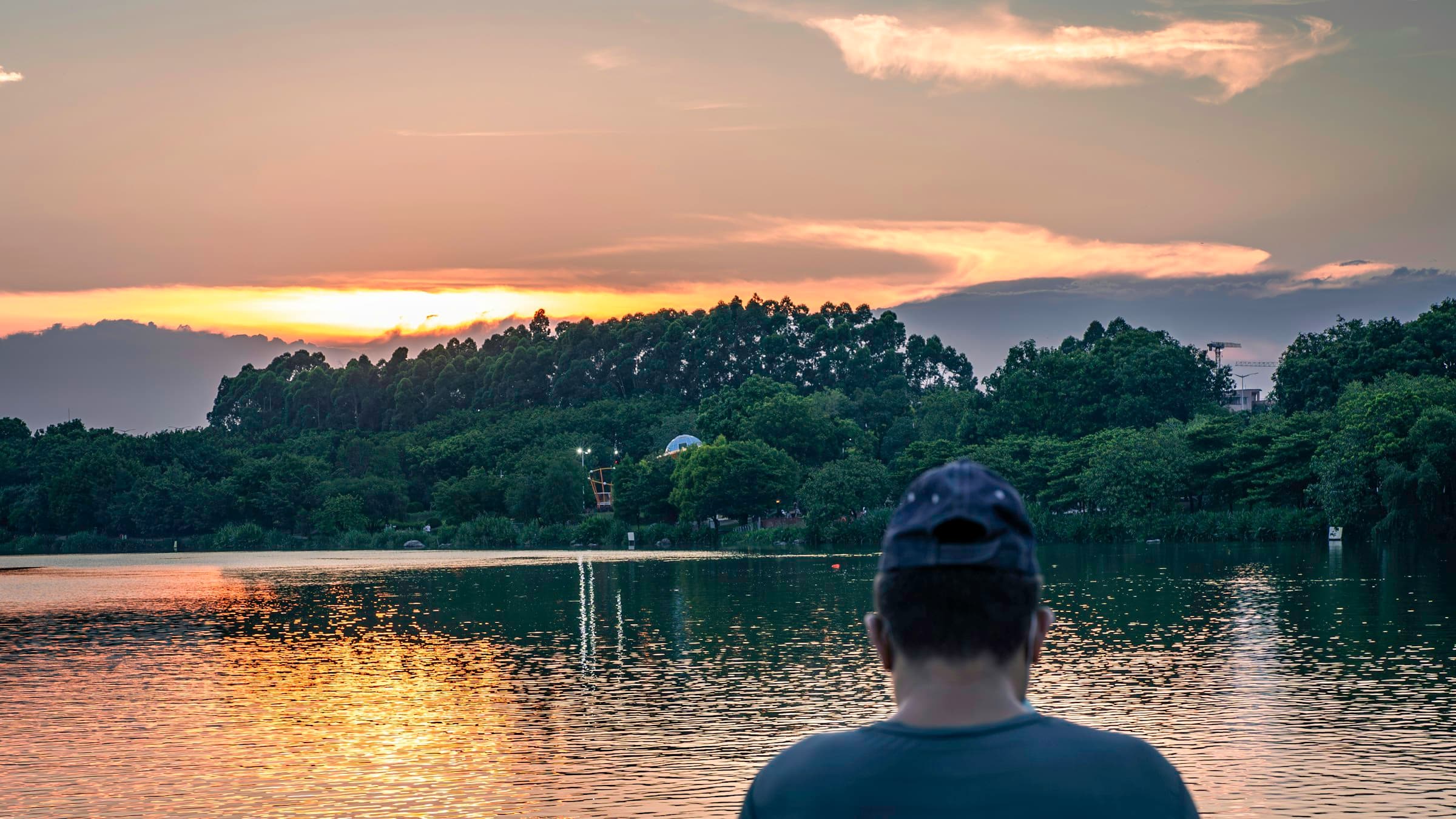 Una persona meditando tranquilamente frente a un lago al atardecer, rodeada de montañas y naturaleza serena.