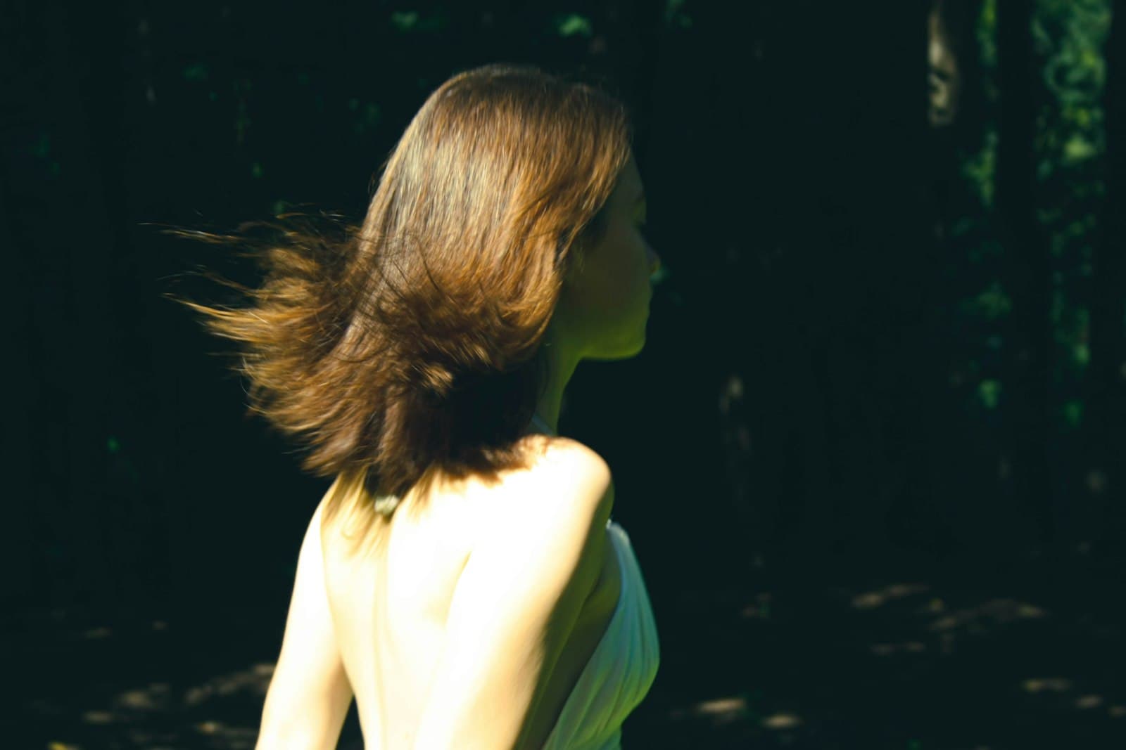 Una mujer camina por un sendero boscoso, envuelta en la luz del sol que se filtra entre los árboles.