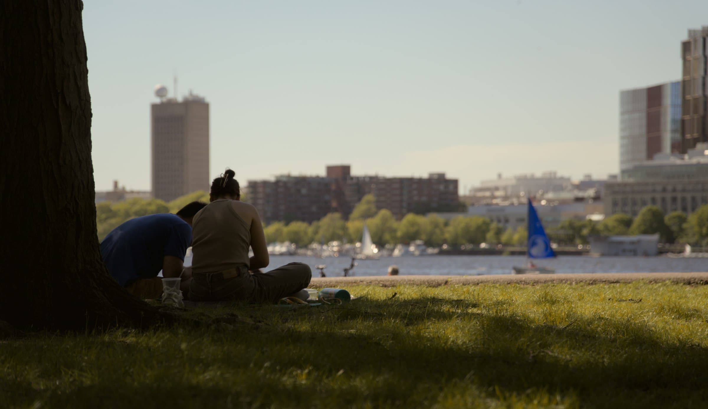 Una persona sentada en un parque urbano, con edificios al fondo, meditando o en un estado de calma