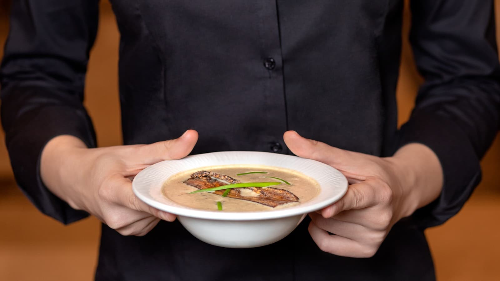 Manos sosteniendo un tazón humeante de sopa en un ambiente cálido