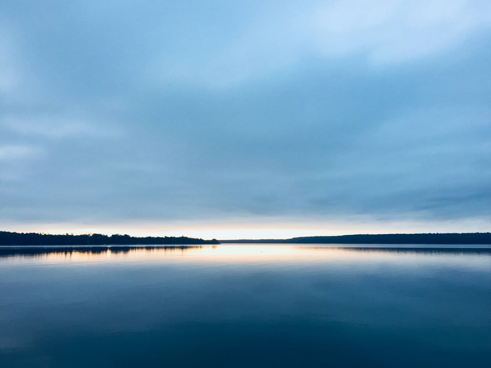 Un lago en calma al amanecer, con niebla suave sobre el agua, transmitiendo una sensación de paz.