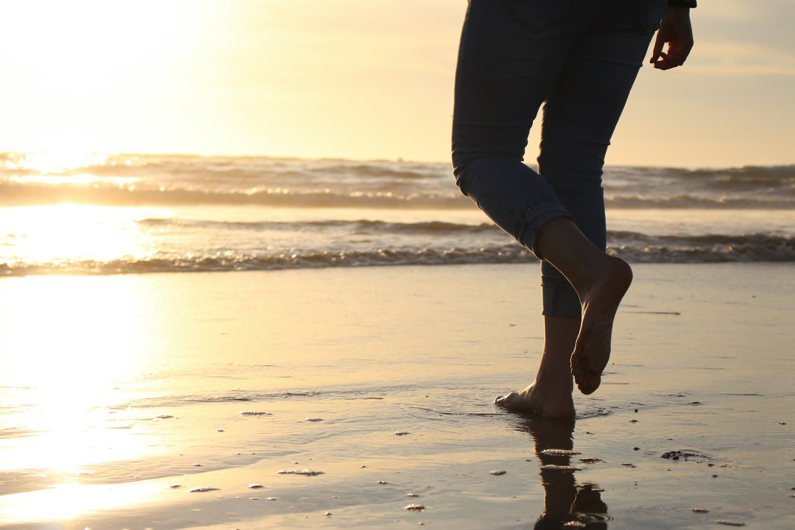 Persona caminando descalza por la orilla de la playa al amanecer