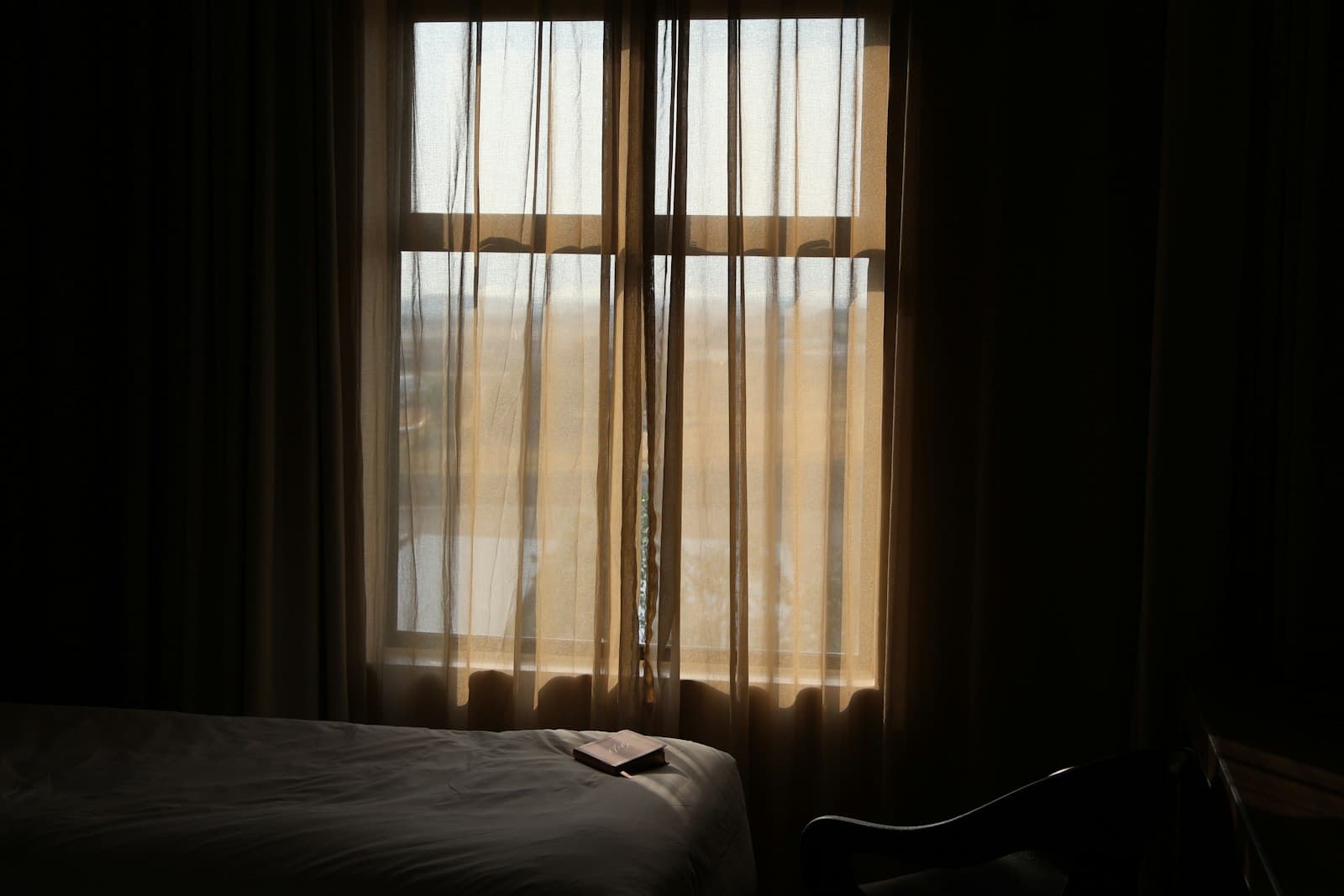 Una ventana abierta con cortinas suaves y luz natural entrando en un dormitorio acogedor