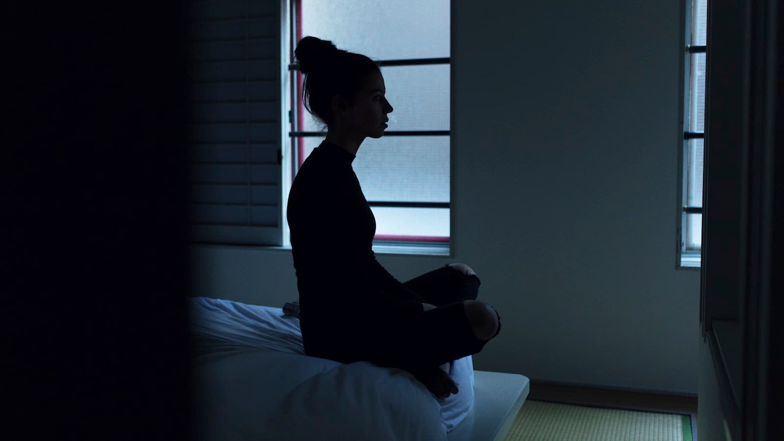 Persona sentada en la cama meditando tranquilamente en la luz de la mañana