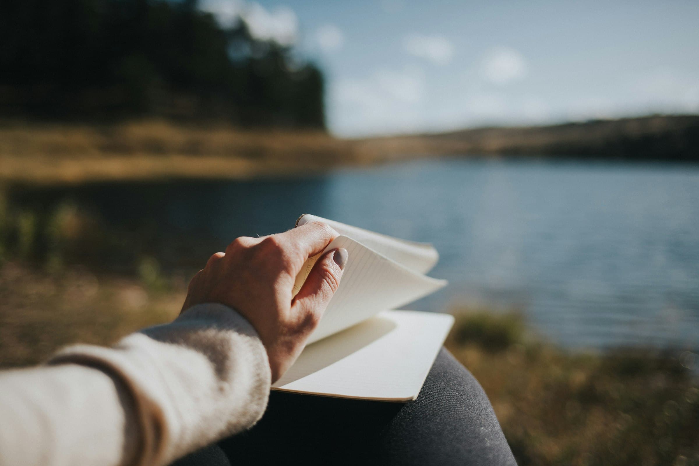 Una persona escribiendo en un diario con un paisaje natural de fondo, transmitiendo serenidad.