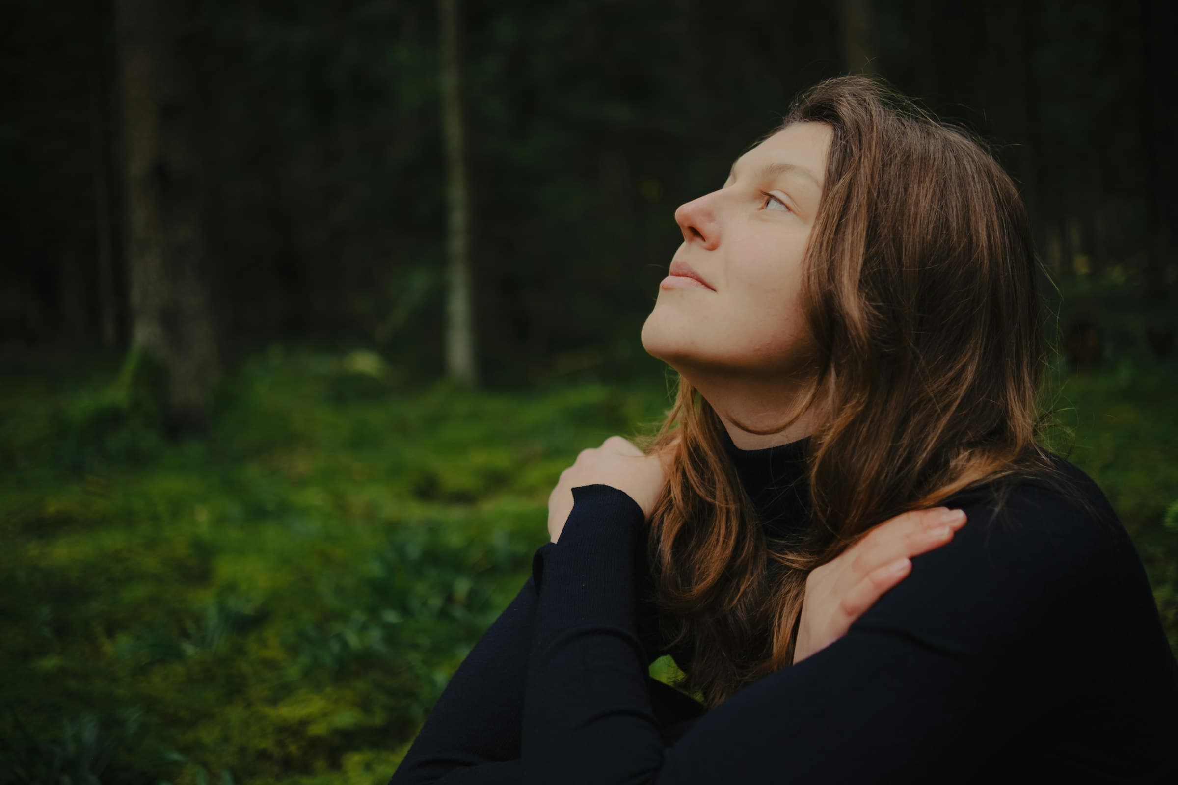 Una persona sentada tranquilamente en la naturaleza, respirando profundamente con los ojos cerrados