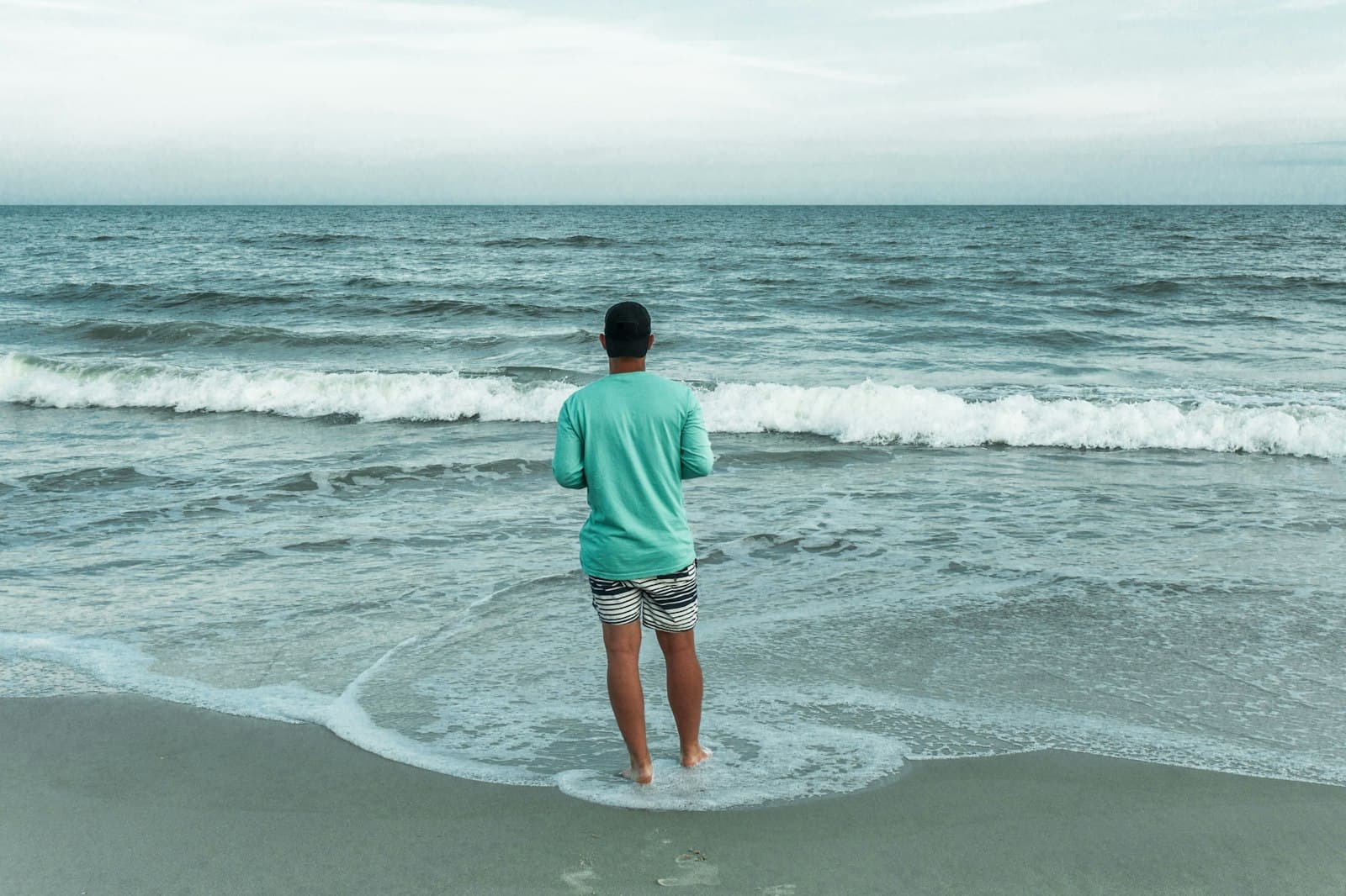 Una persona sentada tranquilamente en la orilla del mar, observando las olas, con una sensación de paz.